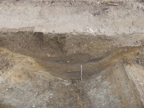 Vue en coupe du large fossé où apparaissent les différentes strates de comblement et quelques éléments de terre cuite (PAVO, 2023)